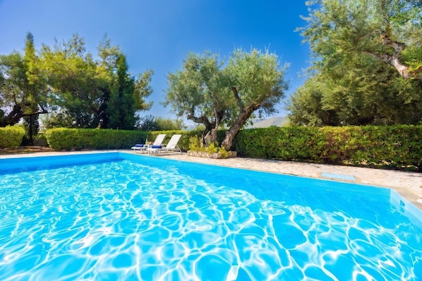 A clear swimming pool with lounge chairs and trees around.