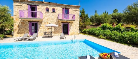 A stone building with a swimming pool, two balconies, and outdoor seating.