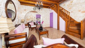 A cozy living room with a stone wall, wooden furniture, a chandelier, and a staircase. - Villa Carolina - Two Bedroom Villa, Sleeps 5 (Agios Dimitrios)