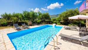 A rectangular swimming pool with clear blue water, surrounded by lounge chairs and a stone patio. - Villa Carolina - Two Bedroom Villa, Sleeps 5 (Agios Dimitrios)
