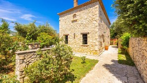A stone house with a tiled roof, a paved pathway leading to the entrance, and a stone wall on one side.