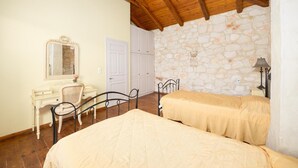 A bedroom with two beds, a dresser, a mirror, and a stone wall.