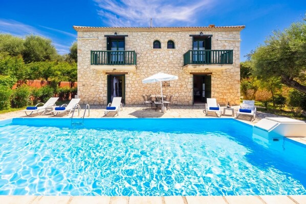 A stone building with a pool, outdoor seating, and a clear blue sky.
