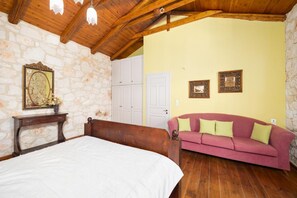 Un dormitorio con techo de madera, paredes de piedra, una cama, un sofá rosa y una puerta blanca.