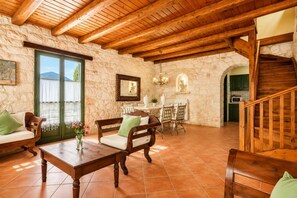 A rustic interior with stone walls, wooden beams, a dining area, and a staircase.
