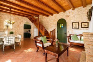 A rustic interior with a wooden staircase, stone walls, a dining area with a table and chairs, and a green door.