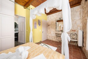A bedroom with a bed, a chair, a mirror, and a stone wall.