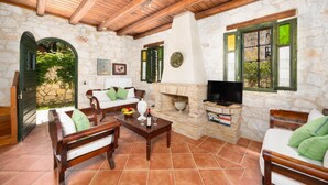 A cozy living room with stone walls, wooden furniture, a fireplace, and a television.