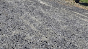 Uma estrada de cascalho leva a uma casa com varanda coberta.