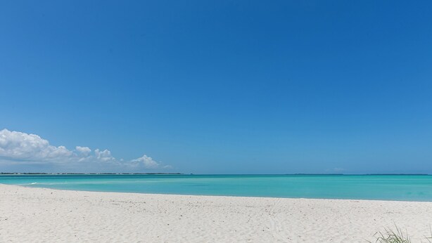 A beach with white sand and clear turquoise water under a blue sky.