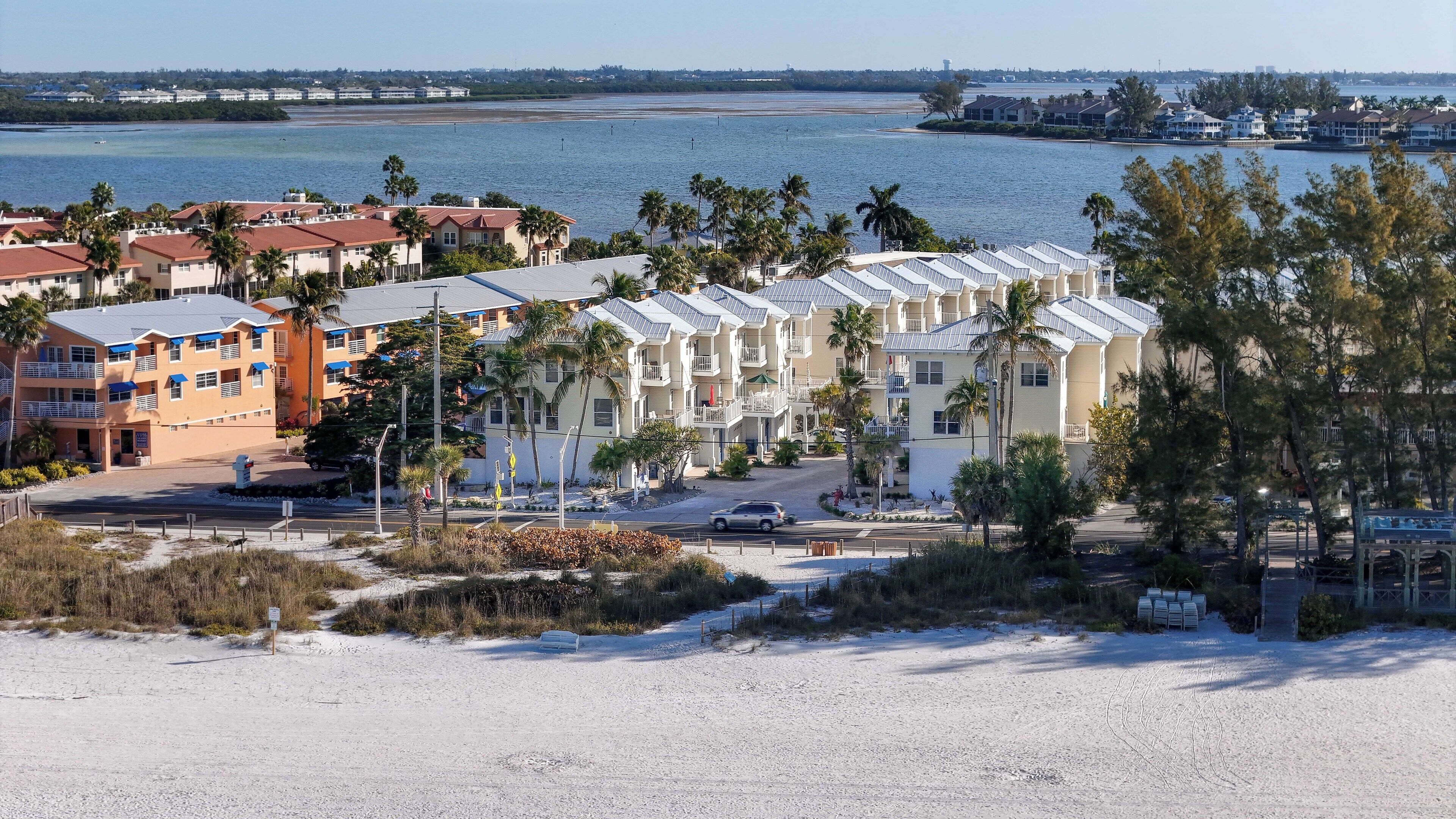Un hôtel situé sur la côte, composé de plusieurs bâtiments à étages, avec une plage de sable au premier plan et une vue sur l’océan.