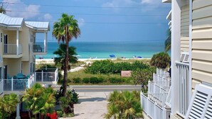 A beachfront property with multiple balconies overlooking the ocean, a sandy beach with umbrellas, and a clear view of the sea.