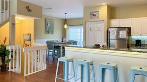 Une cuisine moderne avec des meubles blancs, un réfrigérateur en acier inoxydable et des tabourets de bar bleu clair.