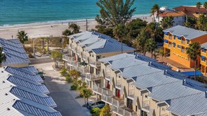 A beachfront hotel with multiple-story buildings, solar panels on the roofs, and a beach view.