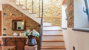 Uma escadaria com paredes de pedra e piso de madeira, levando a um espaço com cozinha.