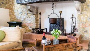 Um interior rústico com parede de pedra, um banco de madeira, uma mesa com uma garrafa de vinho e um vaso com flores.