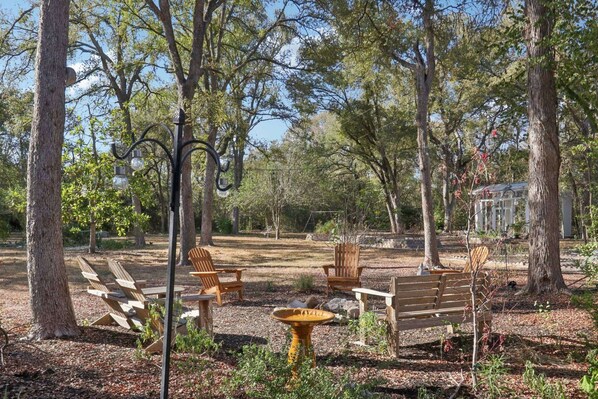 A serene outdoor seating area with wooden benches and chairs, surrounded by trees and a garden.