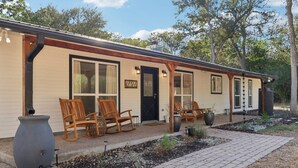 A two-story building with a porch, wooden chairs, and a large planter. - Peaceful Country Escape on 5 Acres with Game Room, BBQ & Outdoor Living (Manor)