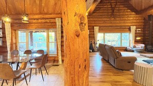 Interior espaiós d'una cabana de fusta amb zona de menjador, saló amb sofàs i grans finestres que donen vistes a l'exterior.