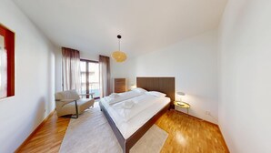 Una camera d'albergo moderna con un letto grande, una poltrona, un comodino con una lampada e vista sulla città.