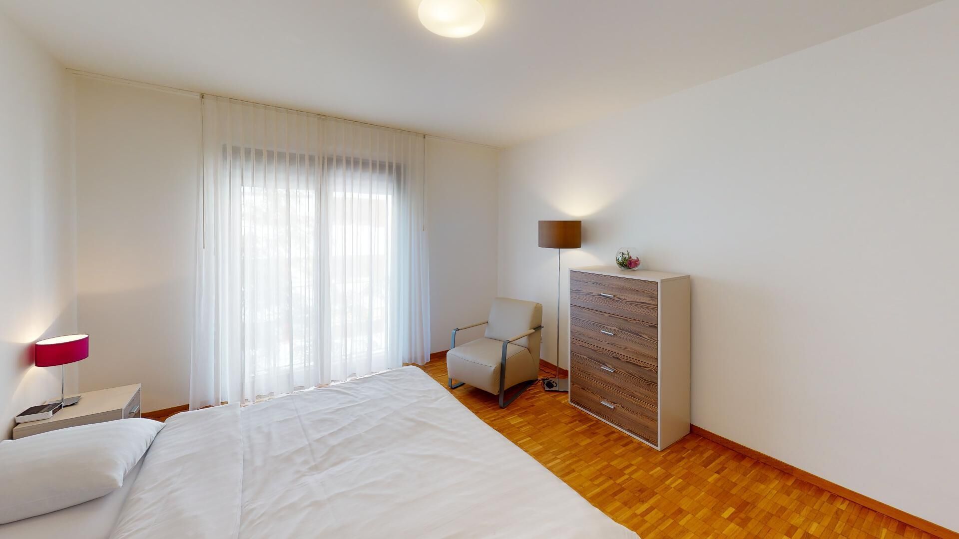 A bedroom with a bed, a chair, a dresser, and a lamp.