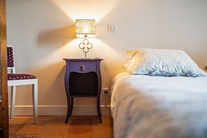 Ein Schlafzimmer mit einem Bett, einem Nachttisch mit Lampe, einem Stuhl und einer Steckdose.