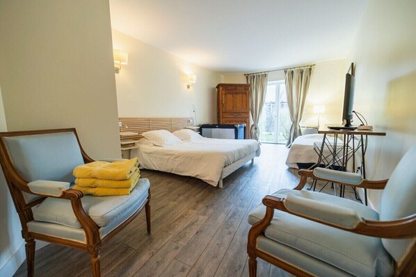 A hotel room with a bed, two armchairs, a desk with a computer, a wooden cabinet, and a window with curtains.