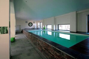 Ein moderner, überdachter Schwimmbereich mit Steinbord, großen Fenstern und schlichtem Interieur.