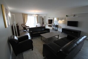 Ein modernes Wohnzimmer mit einer Couch, Sesseln, einem Couchtisch, einem Kamin und einem an der Wand befestigten Fernseher.