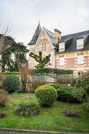 A building with a prominent tower and a well-maintained garden with various shrubs and a neatly trimmed bush.
