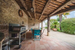 An outdoor patio with a brick wall, wooden ceiling, and a table with chairs.