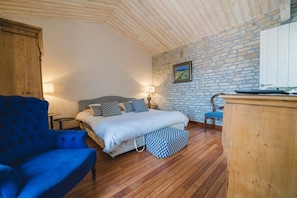 Une chambre à coucher avec un lit, un fauteuil bleu, une commode en bois et un mur en pierre.