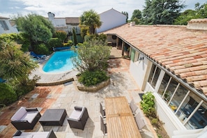 Un jardin avec une piscine, un espace salon extérieur et une maison avec un toit en tuiles.