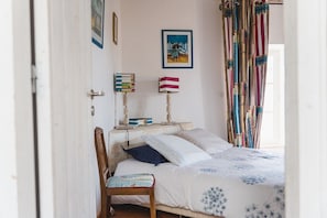 A bedroom with a bed, a bedside table with books, a lamp, and a chair.