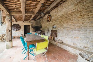 A rustic stone-walled dining area with a wooden table and chairs, a stone fireplace, and a stone bench.