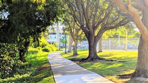 Un sendero bordeado de árboles y césped, que conduce a un edificio con una valla al fondo.