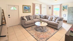 Una sala de estar con un sofá modular, una mesa de centro, una escalera y una puerta con ventanal.