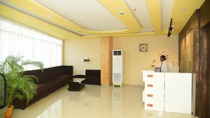 A reception area with a reception desk, a sofa, a coffee table, and a potted plant. - Hotel Bensen (Puri)