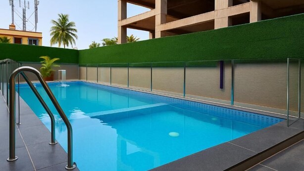 A swimming pool with a metal ladder, surrounded by a green wall and a building in the background. - Hotel Bensen (Puri)