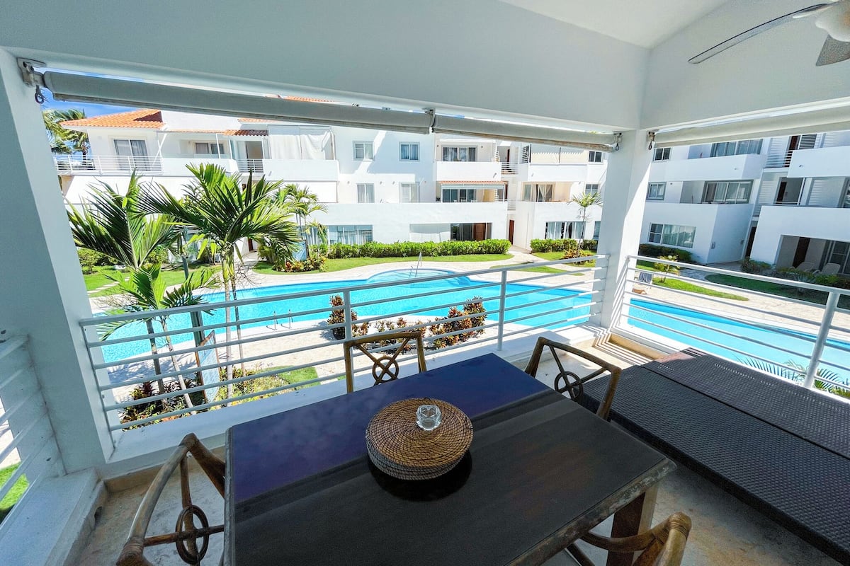Un balcón con vistas a una piscina, edificios blancos y palmeras.