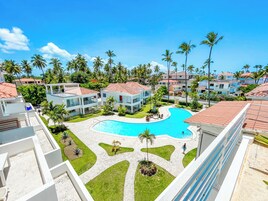 A resort with a central swimming pool, multiple buildings with red-tiled roofs, and palm trees.