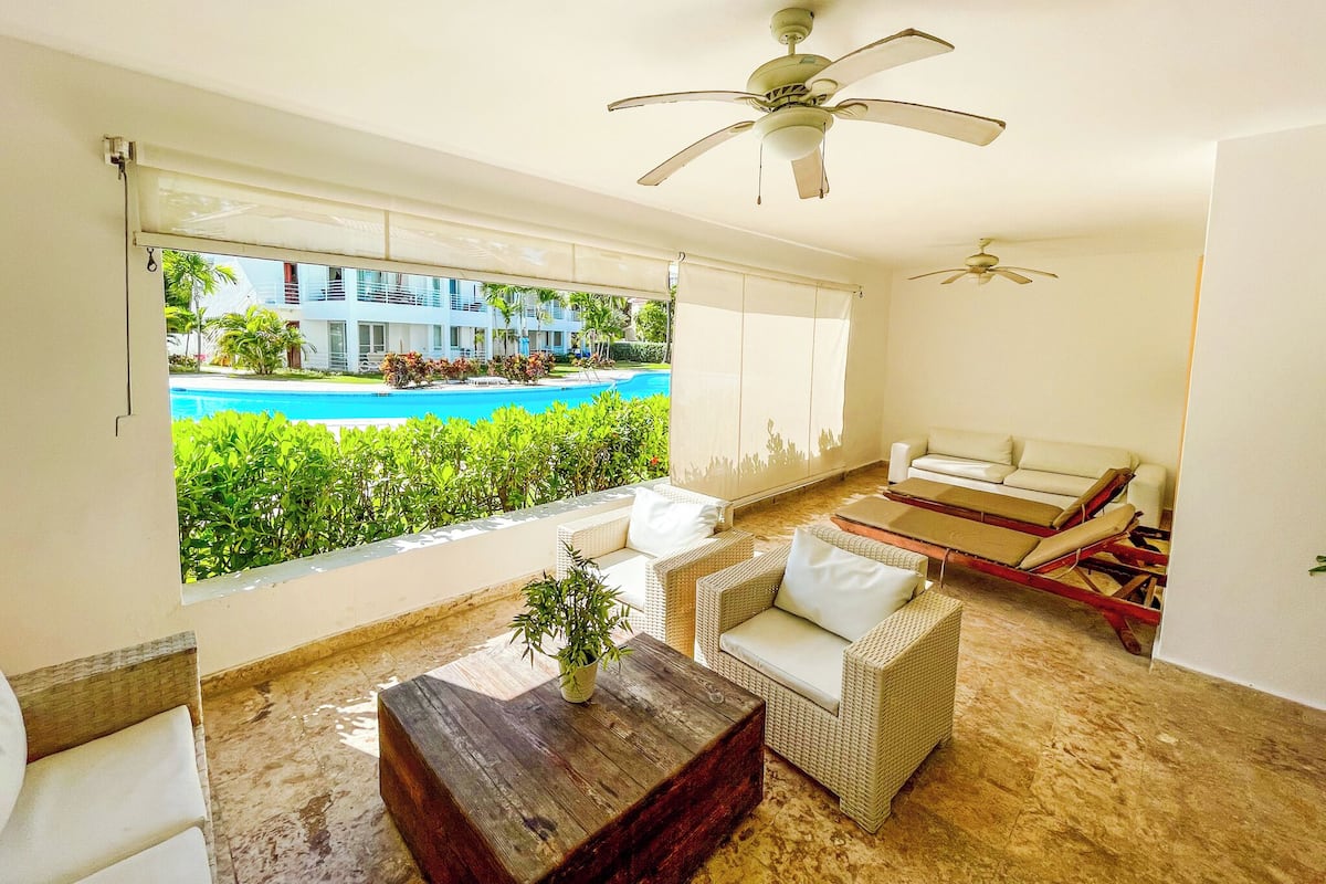Una habitación con vista a una piscina, ventilador de techo, sofá y una mesa de centro de madera.