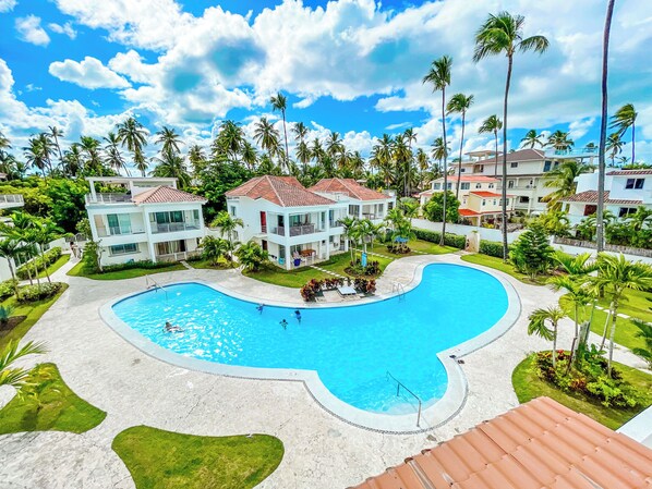 A resort with a large swimming pool, multiple two-story buildings, and palm trees. - KORALES BEACH APARTMENTS (Punta Cana)