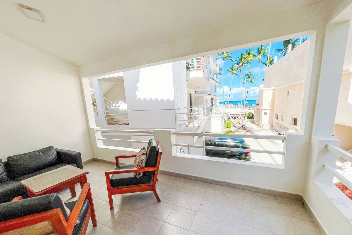 Una habitación con vista a un balcón, una silla, un sofá y suelo de baldosas.