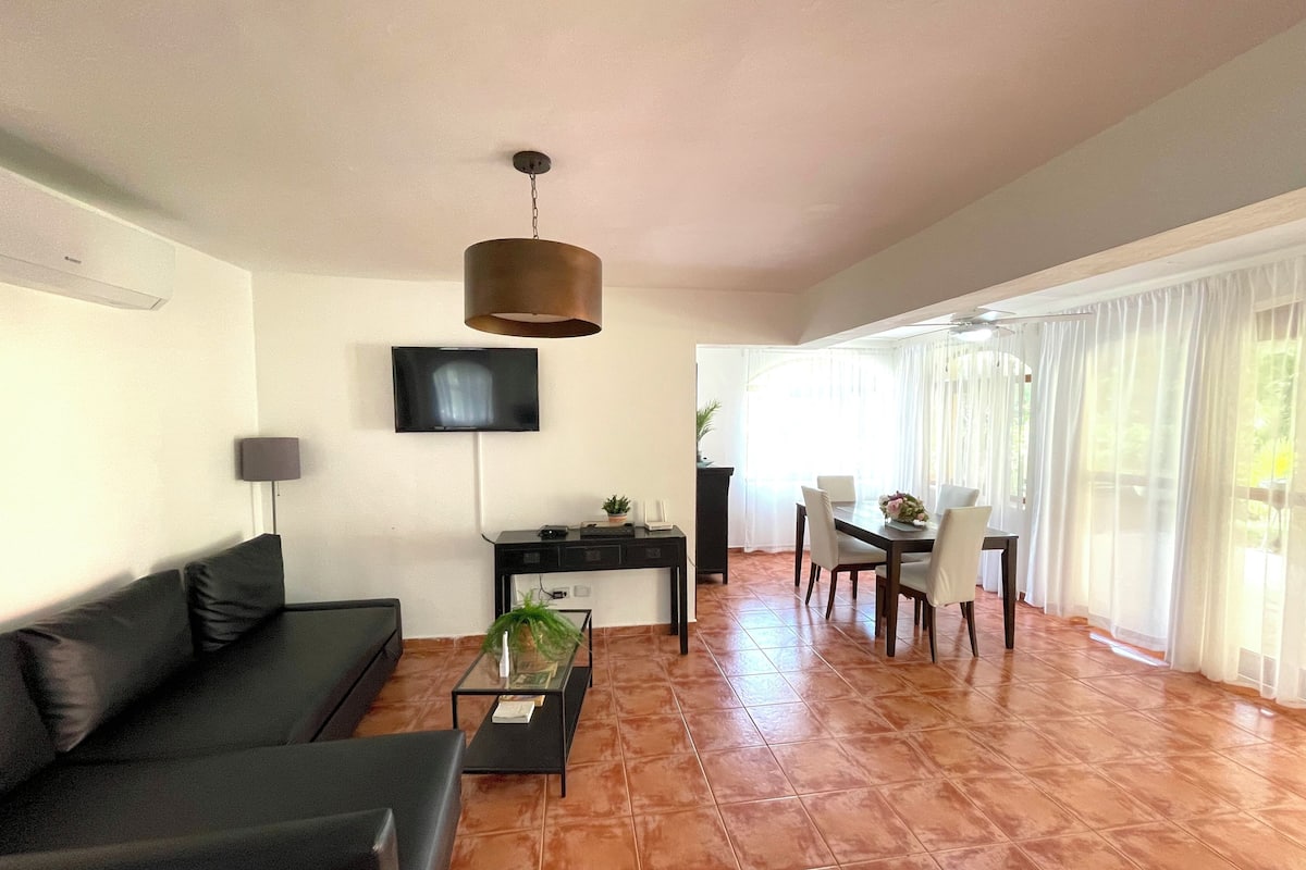 Una sala de estar con sofá, mesa de centro, televisor y un comedor con sillas y mesa.