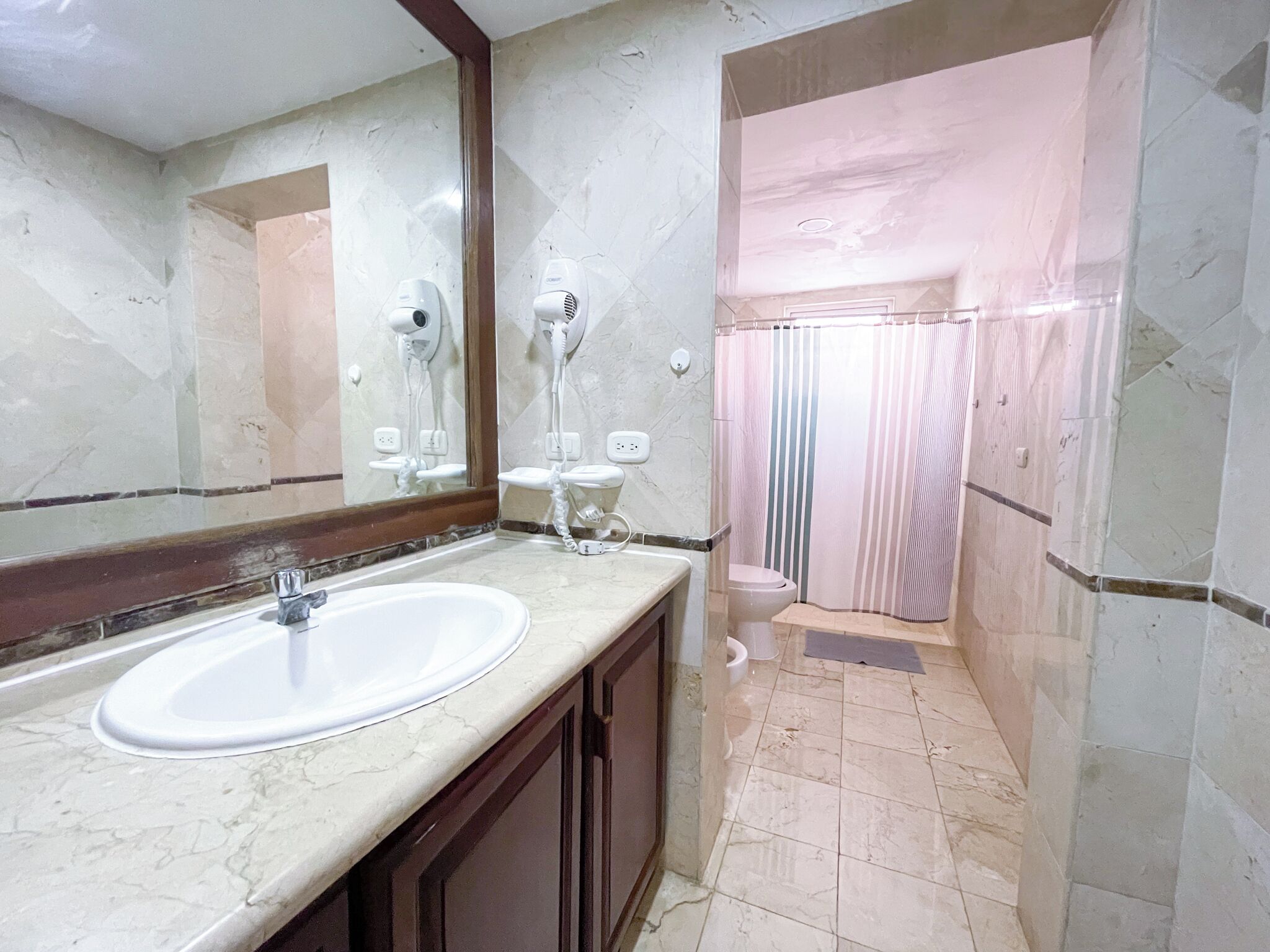 Un baño con lavamanos de mármol, un espejo, ducha con cortina a rayas y un inodoro.
