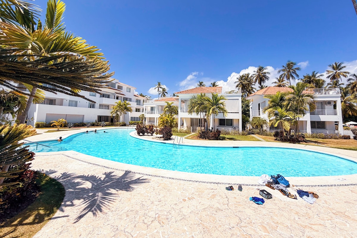 A resort with a swimming pool, palm trees, and modern buildings.
