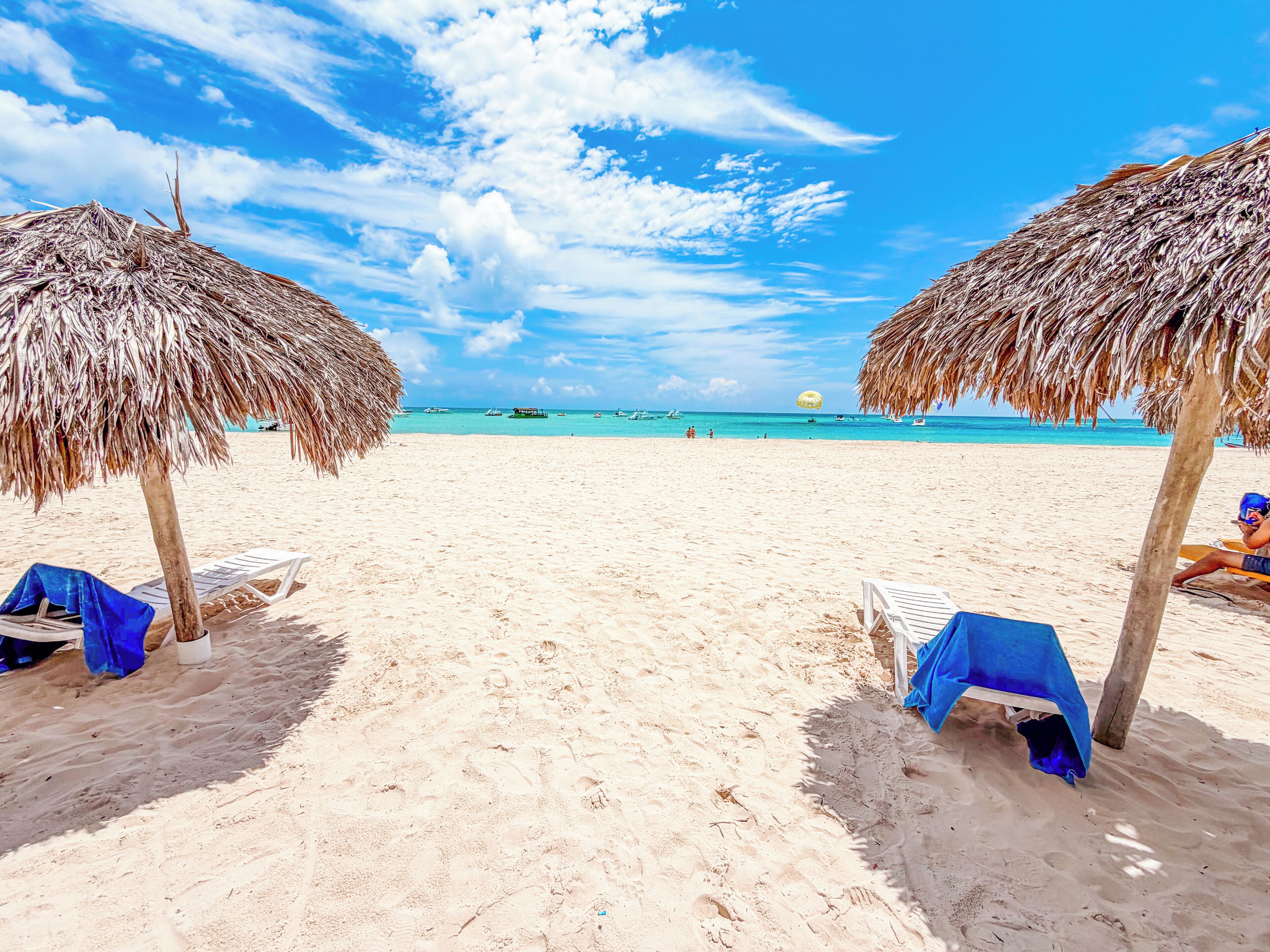 Une plage avec des parasols en chaume et des chaises longues, un ciel dégagé et l’océan en toile de fond.
