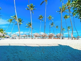 Una playa con palmeras y sombrillas de paja.