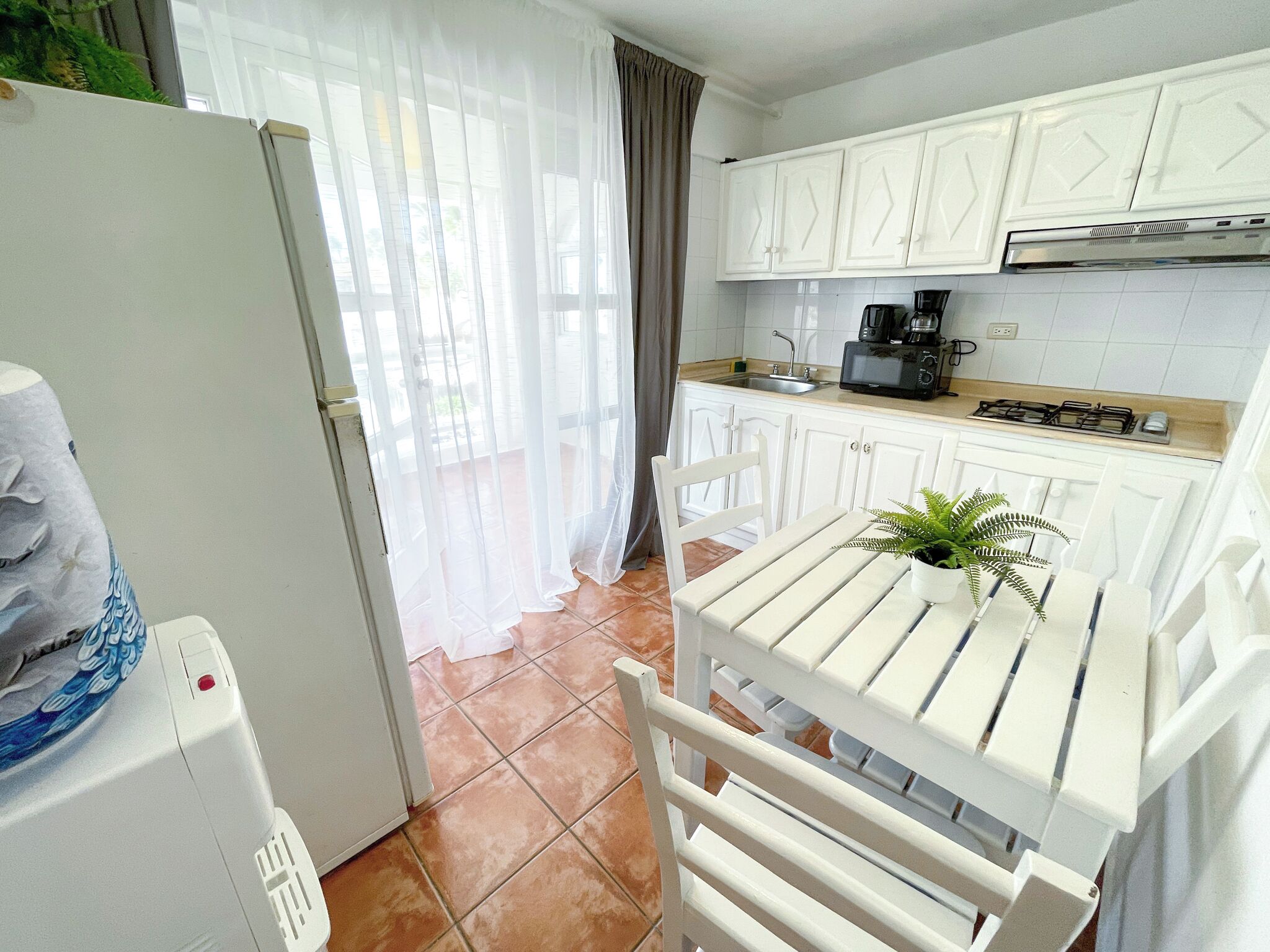 A kitchen with white cabinets, a stove, a coffee maker, and a table with a plant.